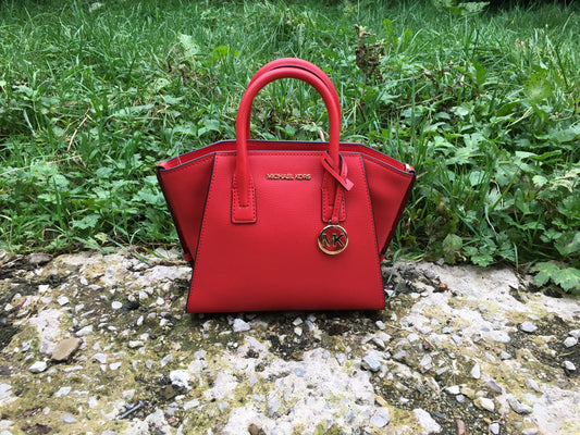 michael kors red avril satchel bag. sitting on a stone patio with grass in background.